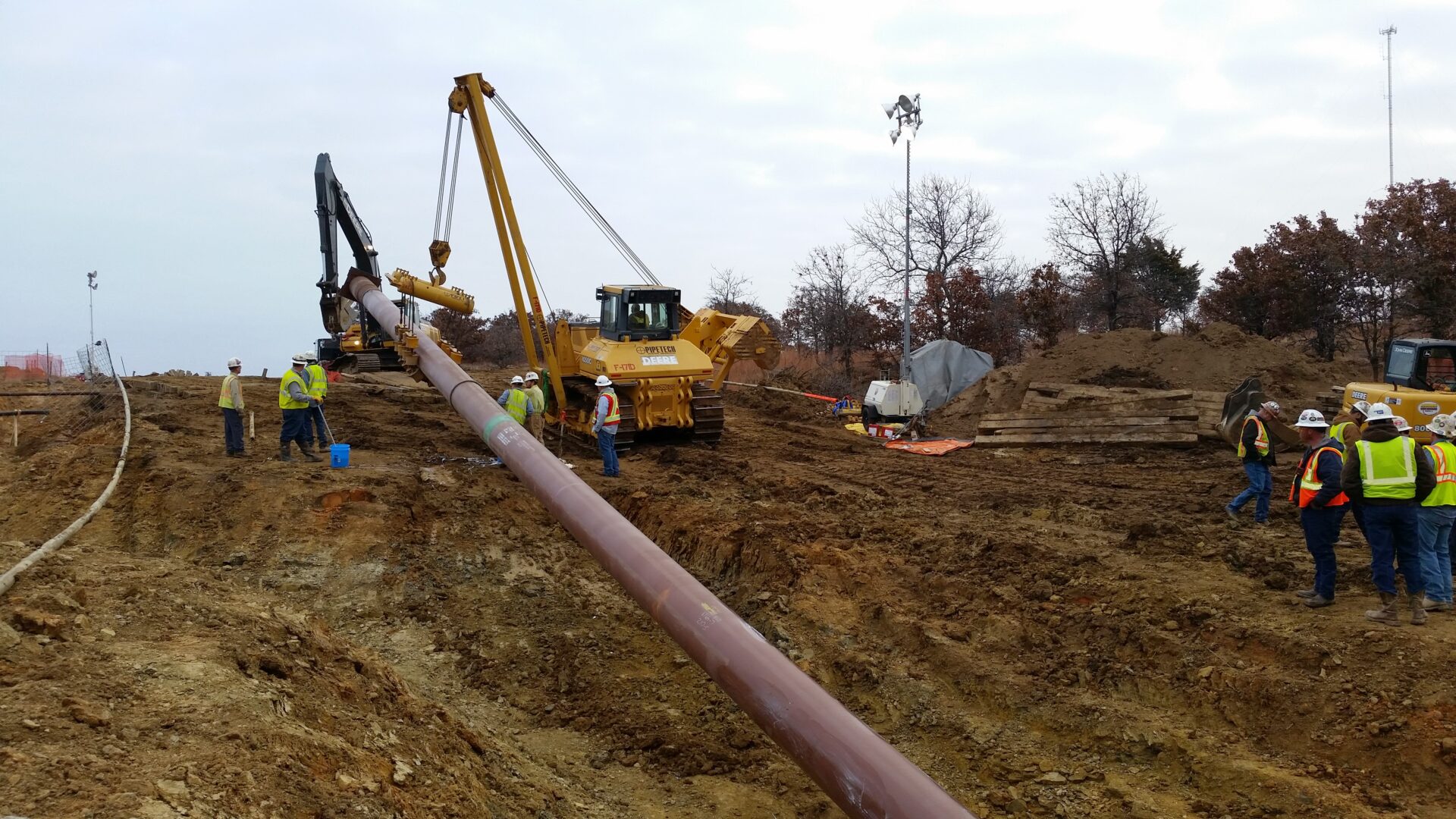A large pipe laying in the ground next to a crane.