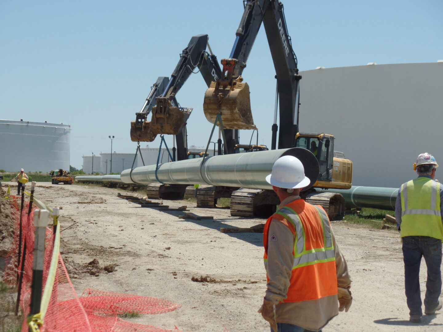 A man in an orange vest and hard hat standing next to a pipeline.